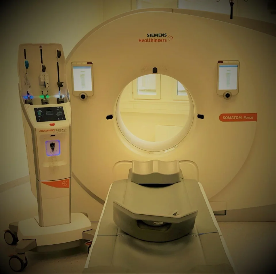 A Bayer MEDRAD Centargo contrast injector with its fluid-loading compartment and controls visible beside a Siemens CT scanner.