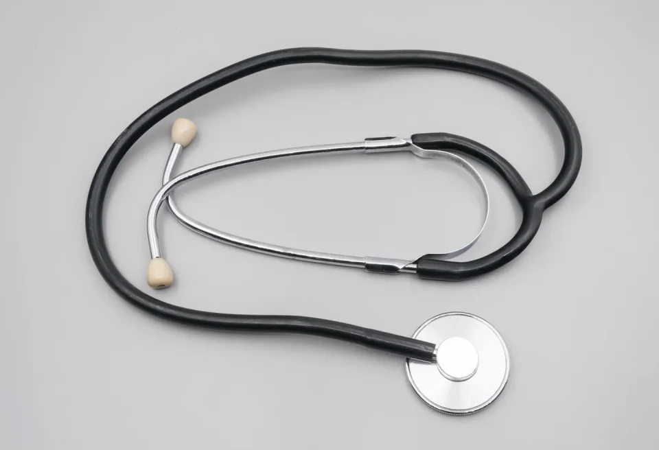 An acoustic stethoscope with black tubing, metal earpieces and a round chestpiece against a light background.