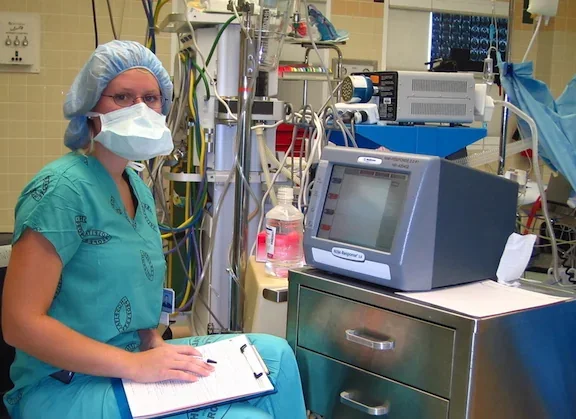 A clinician beside an intraoperative facial-nerve monitoring system in an operating room.
