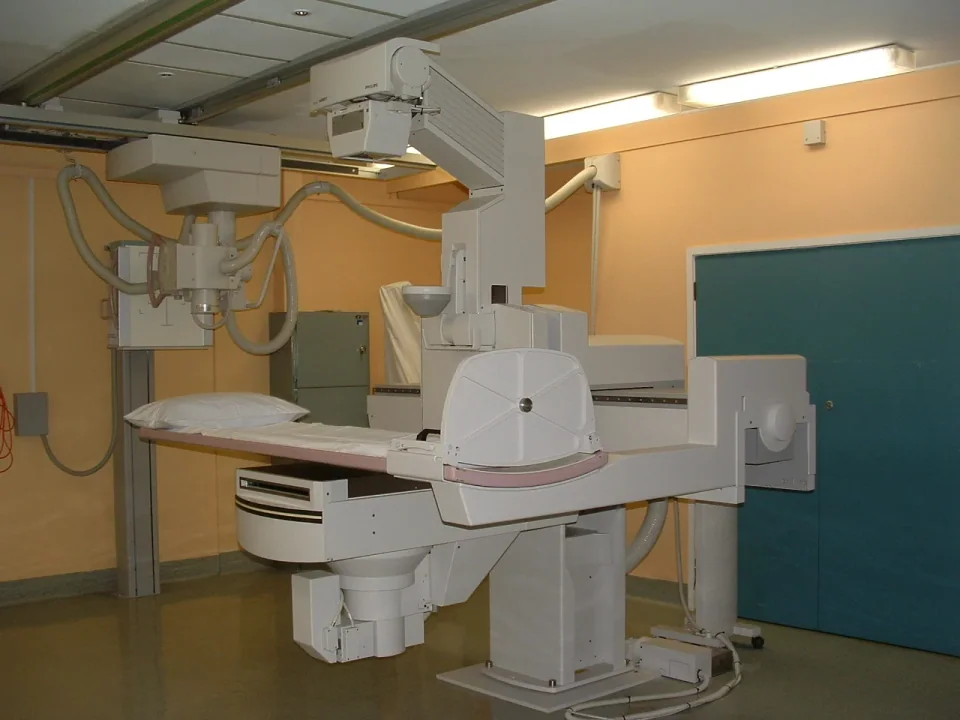 An over-table X-ray tube and fluoroscopy examination table in a fixed imaging room.